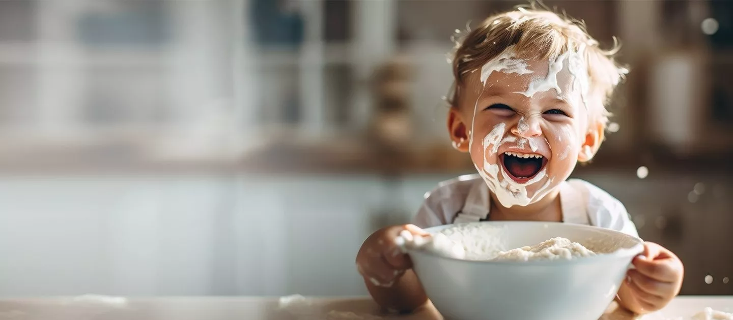 Cute boy laughing over bowl with face covered in food