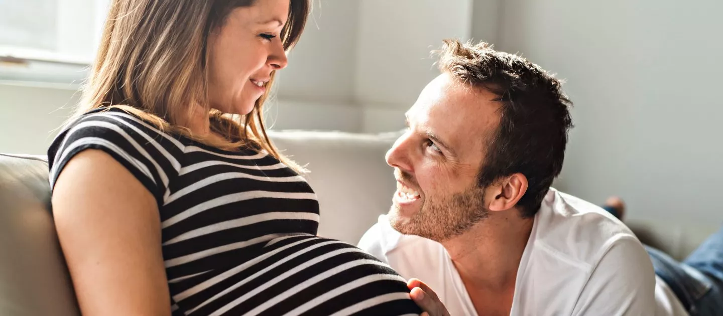 Pregnant couple on couch touching pregnancy belly
